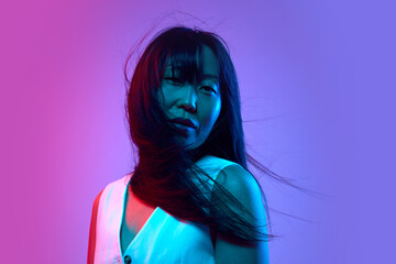 Portrait of attractive and sensual Korean woman in white clothes standing, posing against purple background in neon light. Concept of human emotions, youth, lifestyle