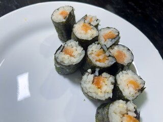 Freshly prepared sushi rolls filled with rice and vibrant orange fish, placed on a white plate.