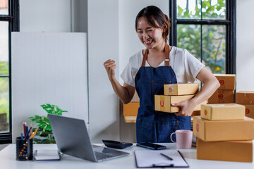 Happy young asian woman startup small business freelance holding parcel box and computer laptop and sitting on chair, Online marketing packing SME box delivery concept