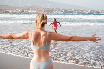Fototapeta premium Mother waiting with open arms for her daughter coming out of the beach to hug her