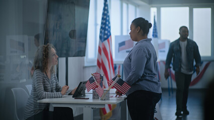 African American woman approaches registration table at polling station. Female polling worker...