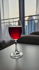 
커튼이 있는 창가와 소파, 흰색 테이블 위 와인잔에 있는 레드와인 또는 과일음료