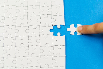 A person is trying to solve a jigsaw puzzle with a hand on a piece