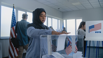 Muslim woman in hijab puts ballot paper in box. Multicultural voters, US citizens vote in voting booths at polling station. National Election Day in the United States. Democracy concept. Slow motion.