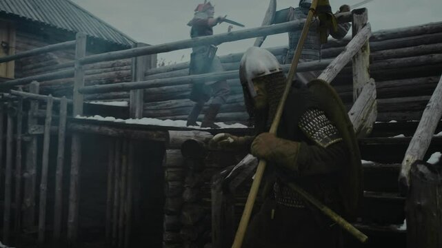 Full tracking shot of medieval Caucasian male warriors in armour, chainmail, helmets, armed with swords, spears, axes, fighting enemy soldiers on battlements of wooden fortress, defending from attack