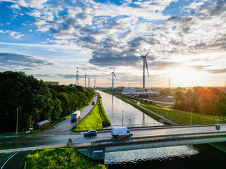 Beautiful sunset view of a canal with wind turbines and vehicles on the road. Renewable energy scenery. © Bjorn B