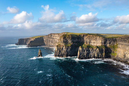 Aerial view of the Cliffs of Moher from the sea, featuring turquoise blue ocean and vivid blue sky