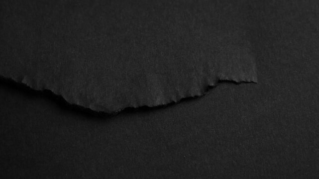 Roughly torn tear of black paper sheet with grainy textures. Monochrome ripped surface. Abstract composition. Rotation