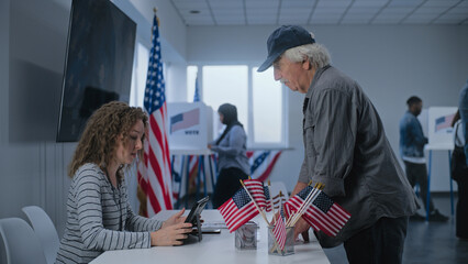 Caucasian mature US citizen stands near registration table at polling station. Female polling...