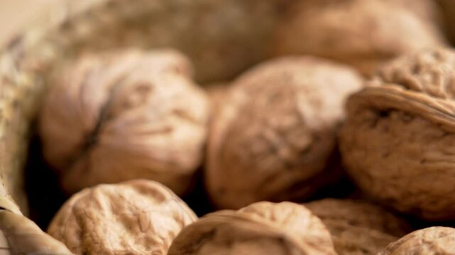 A gourmet hand takes a whole delicious walnut to crack closeup from a rustic wicker bowl. Organic nutritious nuts with textured shell. Macro shot
