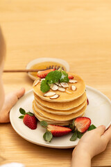 The todler girl holds a plate with delicious pancakes for breakfast at the table. 