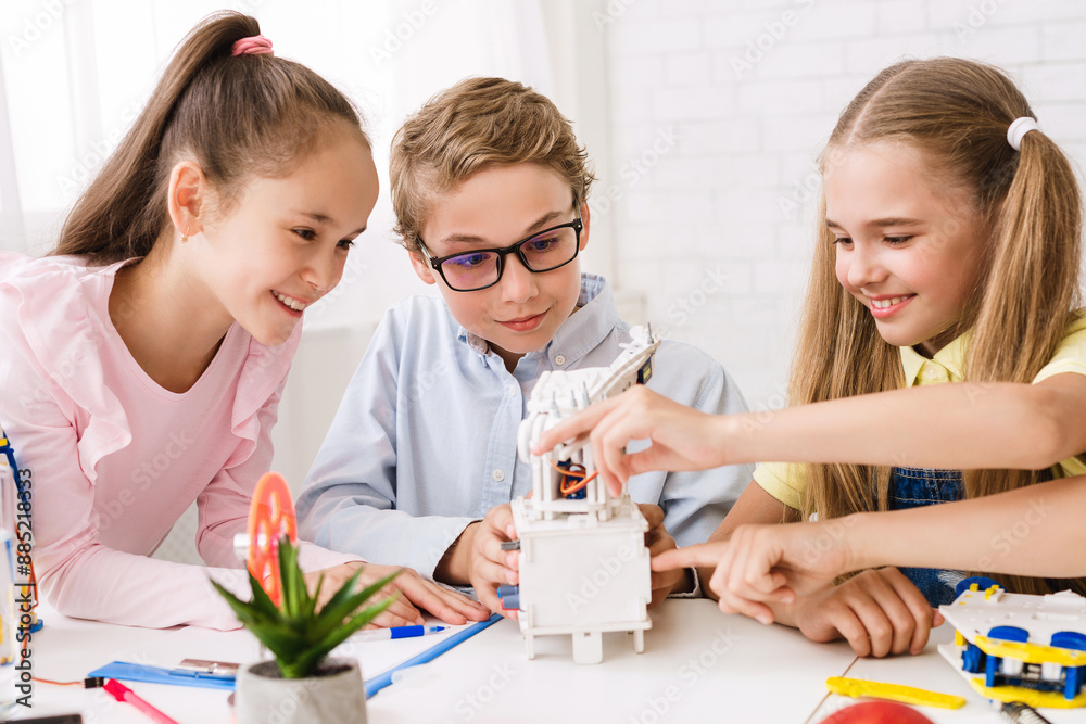 Aufkleber Three children, a boy and two girls, are working together on a robotics project in a classroom setting. They are all focused on the project, and they appear to be enjoying themselves