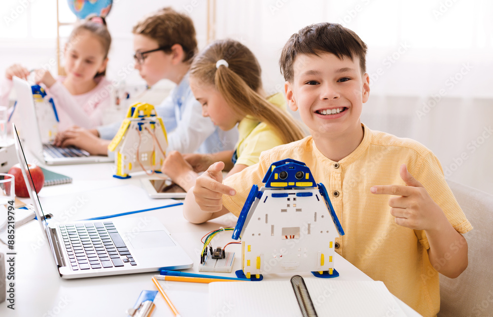 Aufkleber a young boy sits in a classroom, beaming with pride as he points to a robot he built. he is surround