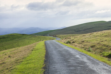 Summer view of tourists walking on curved road with grassland on the hill at Camino de Santiago, St. Jean Pied de Port, France
