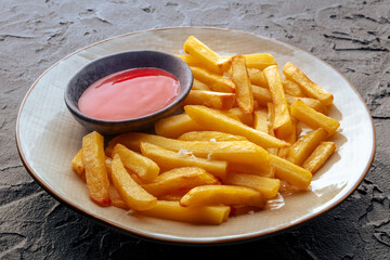 French fries with ketchup, crispy potato chips, on a black stone background
