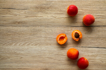 Ripe large apricots on a textured wooden board, one apricot is divided into halves and the pit is visible.