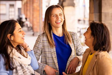 Three women are chatting and laughing happily outdoors, showing joy, happiness, and social interaction among friends