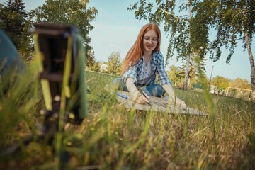 Teenage influencer making protest banner and vlogging through smart phone sitting on grass at park
