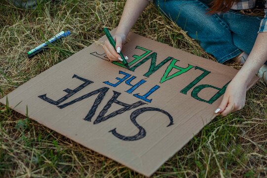 Hands of girl coloring alphabets of protest banner at public park