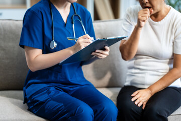 Obraz premium Young Asian nurse attends to older grey-haired mature woman sitting on sofa, conducting health assessment and discussing conditions osteoporosis, arthritis, Alzheimer's disease, dementia, and more.
