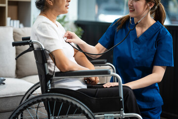 Fototapeta premium A young Asian nurse, the only woman present, assists an older grey-haired mature woman on a wheelchair sitting on a sofa. They focus on taking a medical history and conducting health checks.