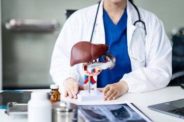A young female nurse works at a desk, discussing liver-related conditions with a grey-haired Asian...
