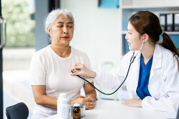 A young female nurse works at a desk with a grey-haired Asian mature woman, discussing...