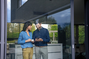 Happy businesswoman standing with businessman using smart phone at home