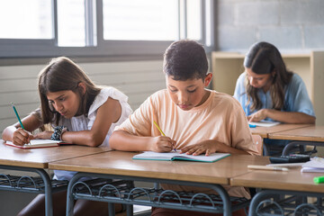 Hispanic primary school boy and girls writing test at desk in classroom at the elementary school - Children Education 