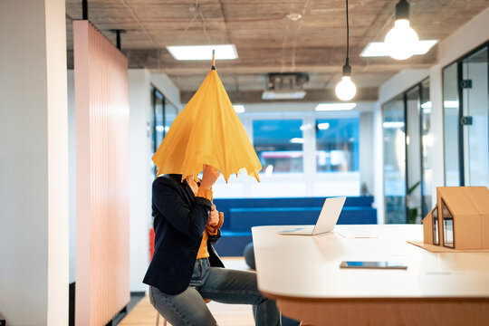 Young businesswoman sitting with umbrella at desk in office