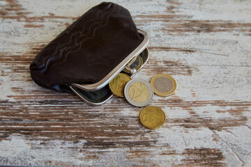 An old wallet with euro coins spilling out of it lies on a worn wooden table, social benefits, austerity, small budget, small pension