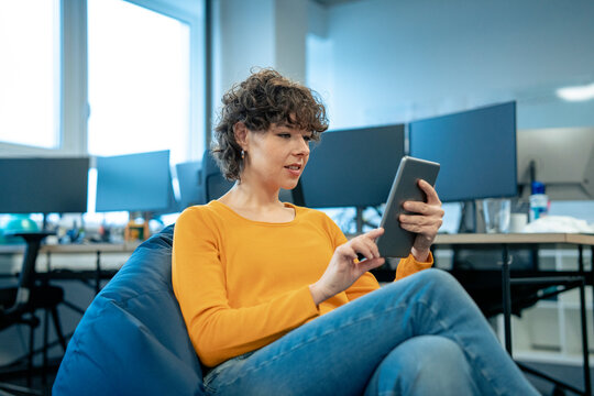Smiling businesswoman sitting on bean bag and using tablet PC at office - Powered by Adobe