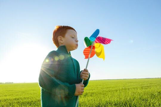 Boy blows multi colored pinwheel toy in field