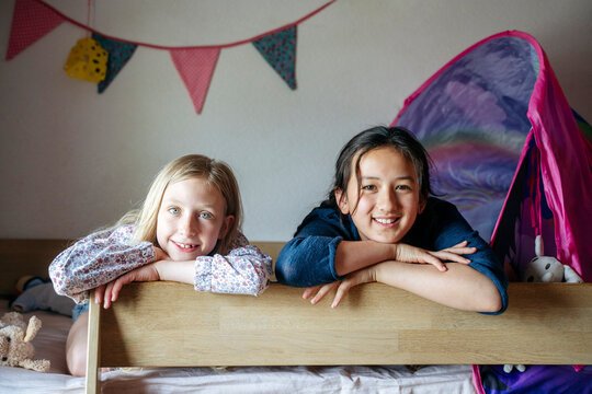 Smiling girls leaning on bunk bed at home