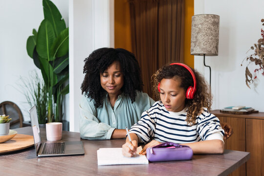 Mother supervising daughter sitting at table doing homework