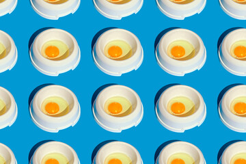 Repetition of dog food bowls with raw eggs on blue background
