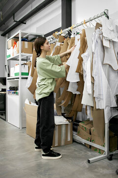 Dressmaker searching for garment templates hanging on rack at workshop