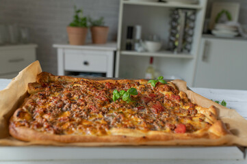 Homemade pizza with minced meat, mozzarella cheese and tomatoes on kitchen counter