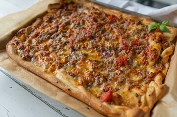 Homemade pizza with minced meat, mozzarella cheese and tomatoes on kitchen counter