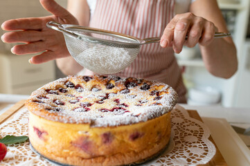 Woman sprinkling powdered sugar over a fresh bake cherry cheesecake