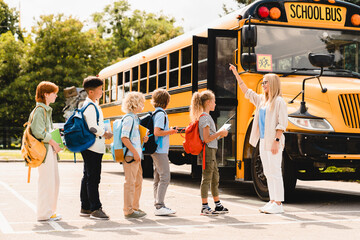 Young teacher counting group of kids pupils schoolchildren before boarding school bus before lessons. Welcome back to school after summer holidays! New educational year semester.