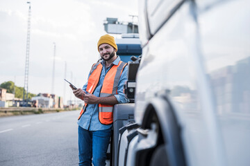 Smiling truck driver leaning on truck with tablet PC