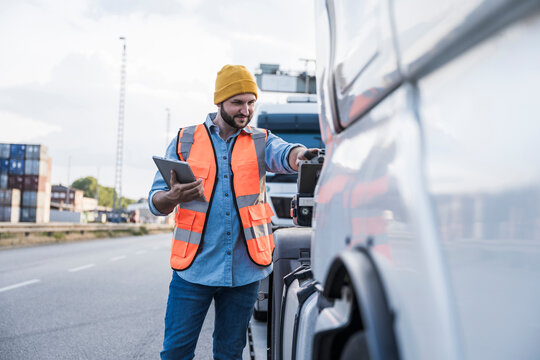 Smiling truck driver examining truck on road