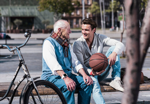 Happy young man holding basketball and talking to grandfather on sunny day