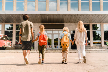 Young parents seeing their kids children to school for lessons classes after summer holidays....