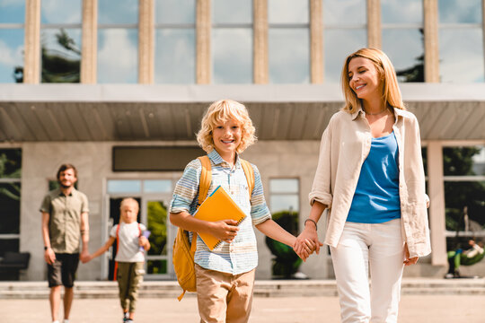 Young parents escorting their kids children from school home after lessons classes after summer holidays. Welcome back to school. New academic educational year semester