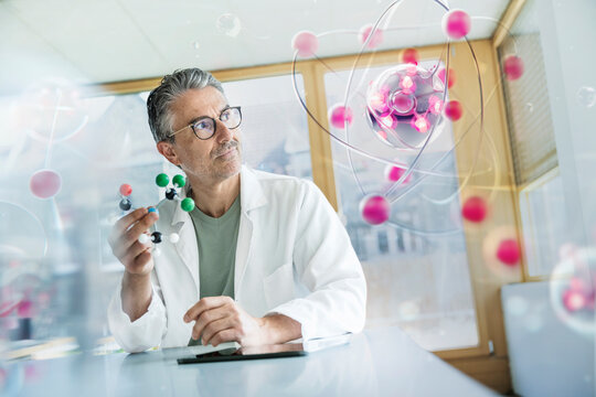 Mature doctor examining molecular structure at desk in hospital office