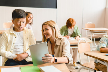 Young teacher tutor helping her students schoolchildren pupils with homework task math exam test at the school lesson class using digital tablet.