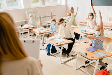 School education during Covid19 pandemic.Schoolchildren students pupils listening to the teacher at lesson class raising their hands in masks. Excellent marks. Attendancy, academic performance concept