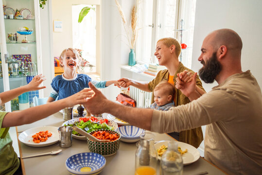 Happy family holding hands and praying at dining table